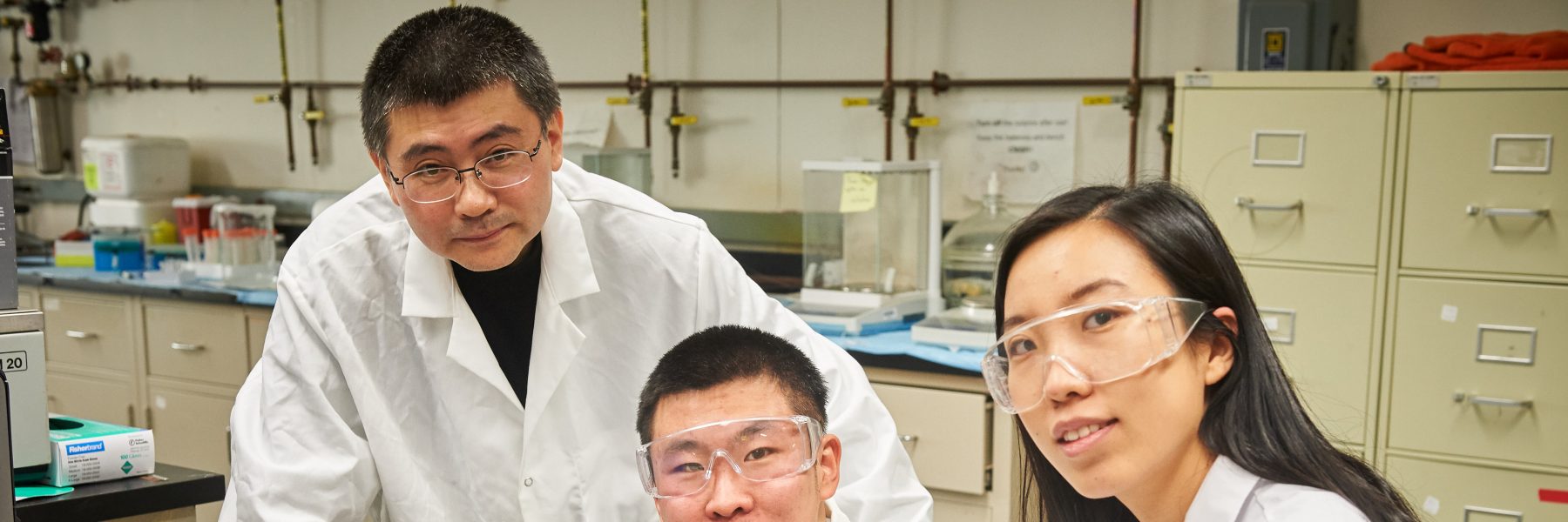 Yu Lei, associate professor of chemical & biomolecular engineering, left, with graduate students Qiuchen Dong and Xiaoyu Ma connect a toxic chemical sensor to a cable in the lab at the United Technologies Engineering Building on Feb. 2, 2016. (Peter Morenus for UConn)